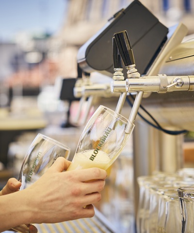Mitarbeiter des Blockbräu zapft frisches Bier direkt vom Zapfhahn in ein Blockbräu Bierglas. Ein zweites Glas hält er zum nächsten Ausschank bereit.