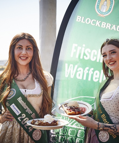 Hamburger Bierprinzessin und Hamburger Bierkönigin 2024 präsentieren frisch gebackene Waffeln auf der sonnigen Blockbräu Hafenterrasse.